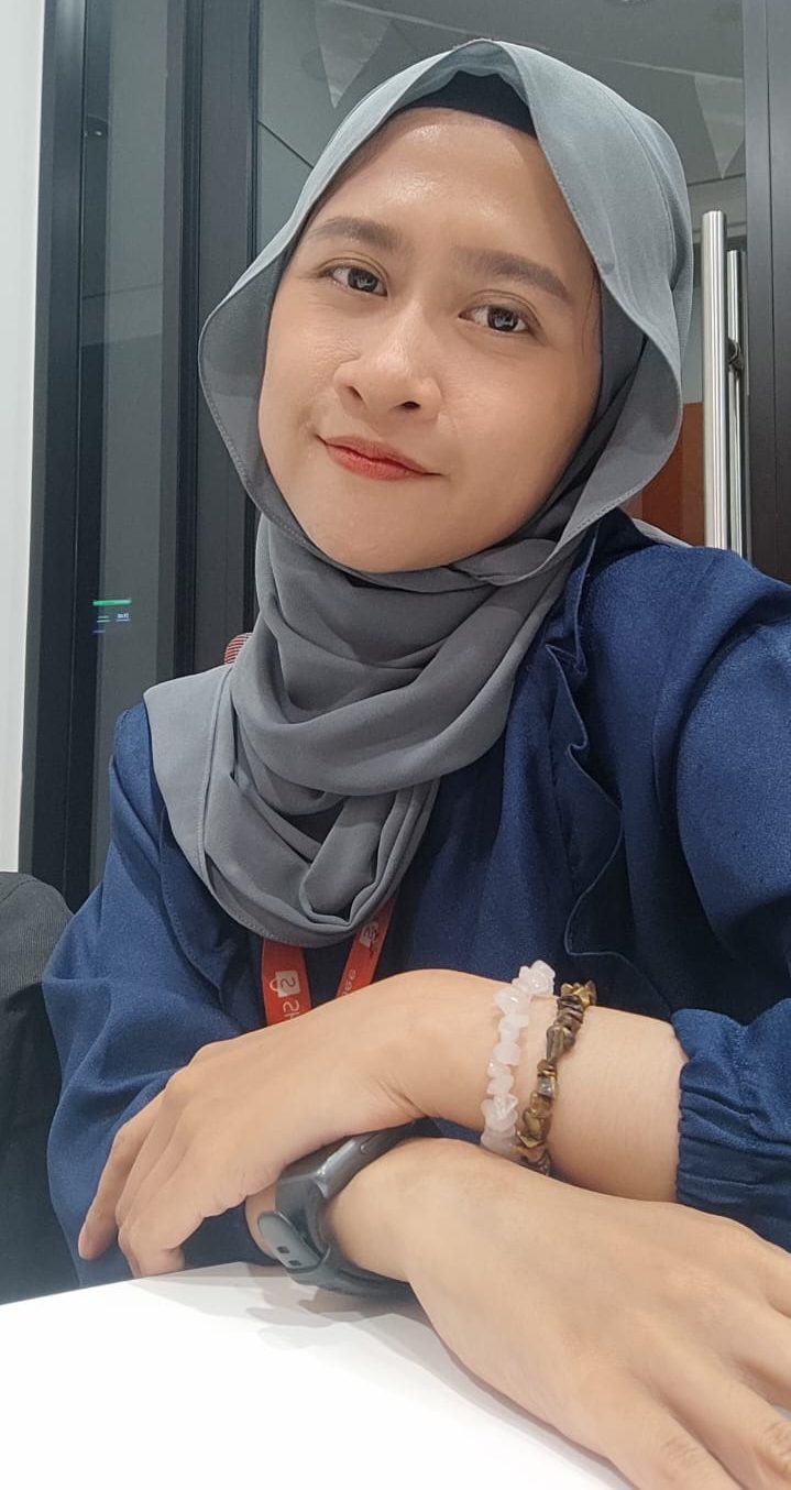 Woman wearing gray hijab and blue outerwear smiling in indoor setting